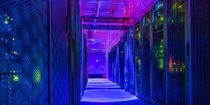 Data center corridor with blue and purple lighting and server racks on both sides.